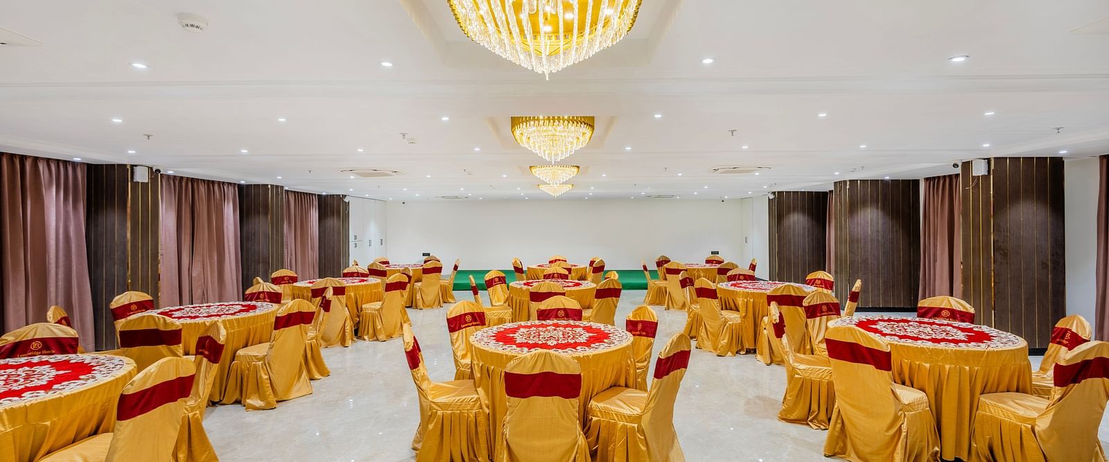 Lemonridge Hotels, KPHB | Banquet hall with round dining tables and chairs, featuring a unique ceiling light.